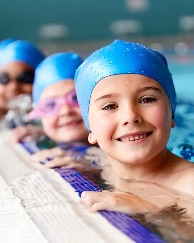 Nens i nenes amb casquet a la vora de la piscina